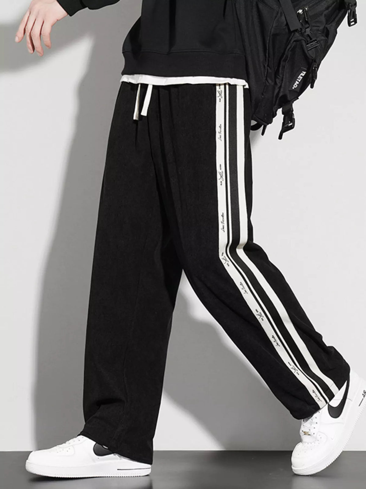 Black loose-fit casual pants with vertical white striped side panels and drawstring waist