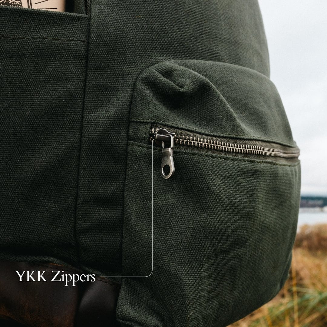 Green backpack detail: front zip pocket with metal zipper pull and visible stitching.