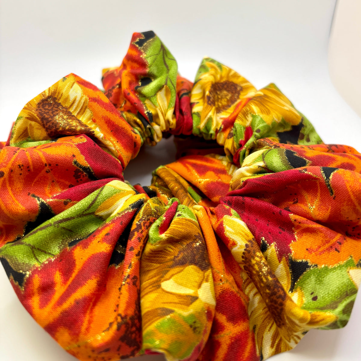 Close-up sunflower and leaf print scrunchie with orange, red, and green gathered fabric