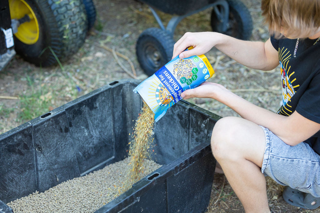 Child pouring shredded herb flakes from a blue pouch into a dark outdoor container