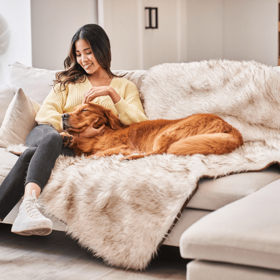 White faux-fur waterproof throw blanket laid across a couch cushion with brown-trim accents