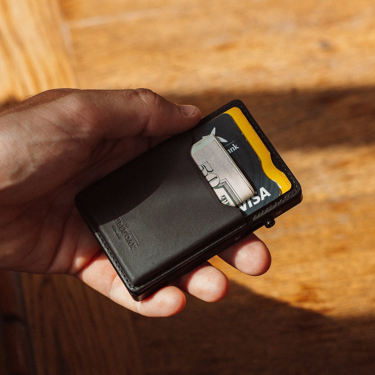 Black leather cardholder wallet with cards and yellow trim, in hand outdoors.