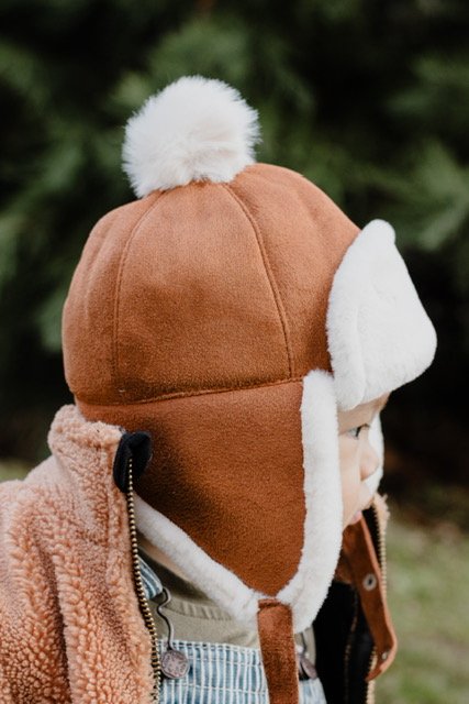 Brown kids trapper hat with white sherpa ear flaps and fluffy top pom-pom