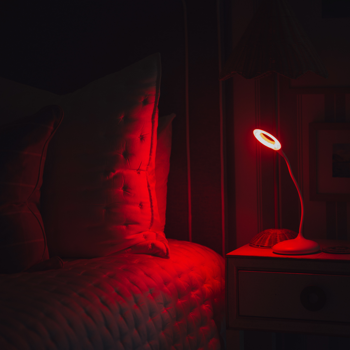 Curved-neck table lamp emitting red night light beside a bed