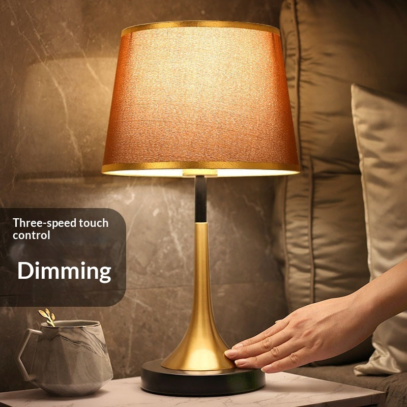 Gold table lamp with amber fabric shade and dark round base, touch-controlled design