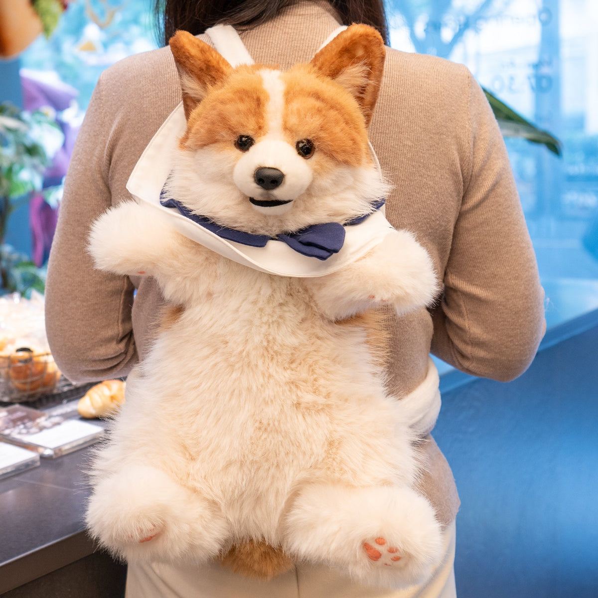 Plush corgi backpack with tan fur and navy bow, worn over shoulders on a person