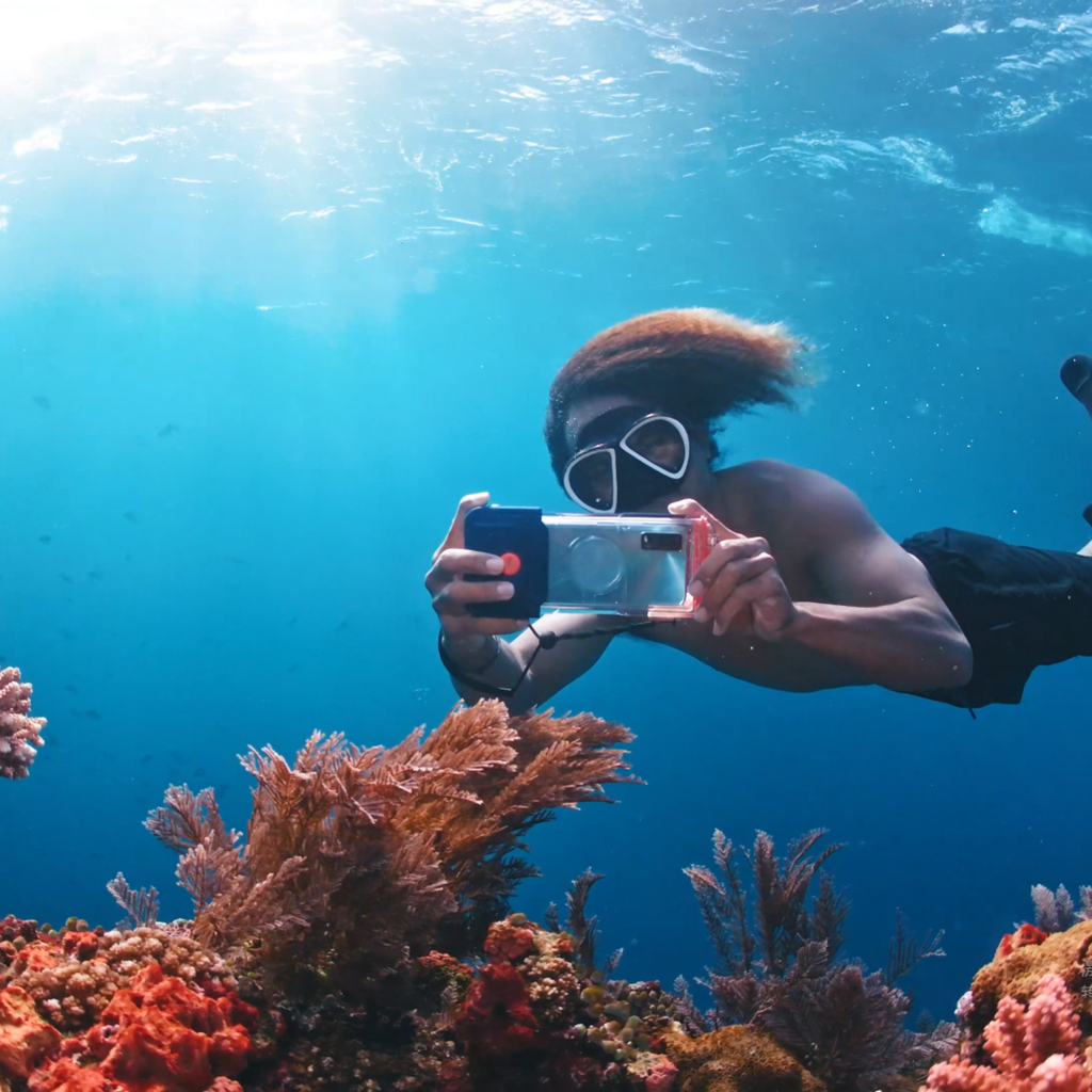 Clear waterproof phone case held in front of a snorkeler, black seal and orange details