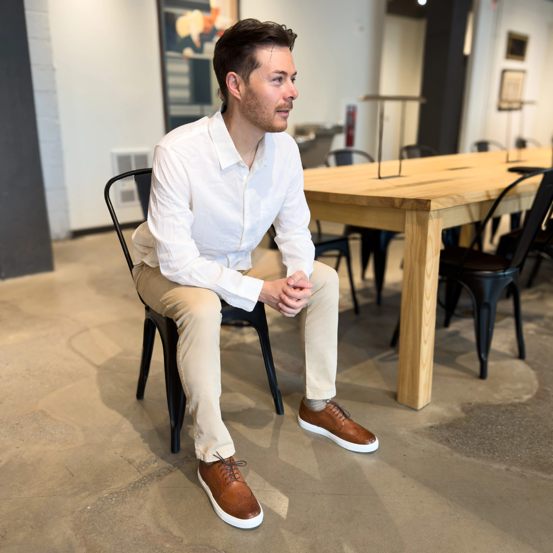 Men's cognac wingtip lace-up shoes with white soles, worn by seated man