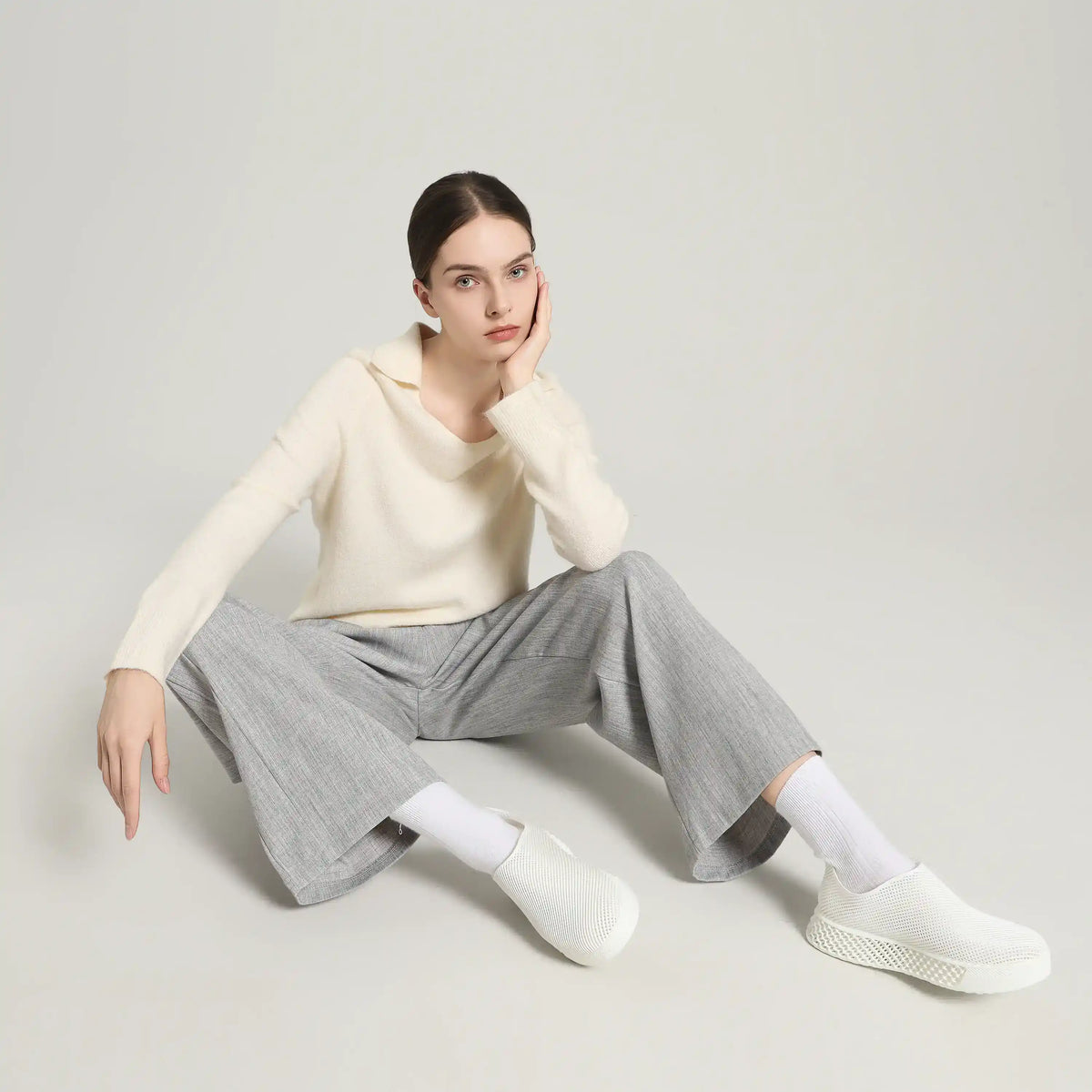 White 3D-printed slip-on sneakers on model seated with gray trousers and socks