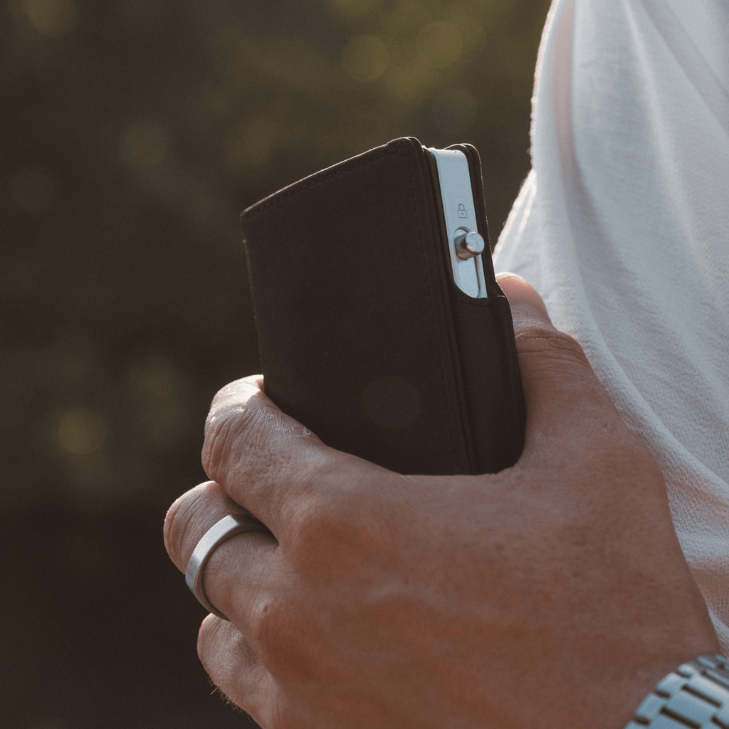 Dark bifold wallet with snap closure, shown in hand from the side