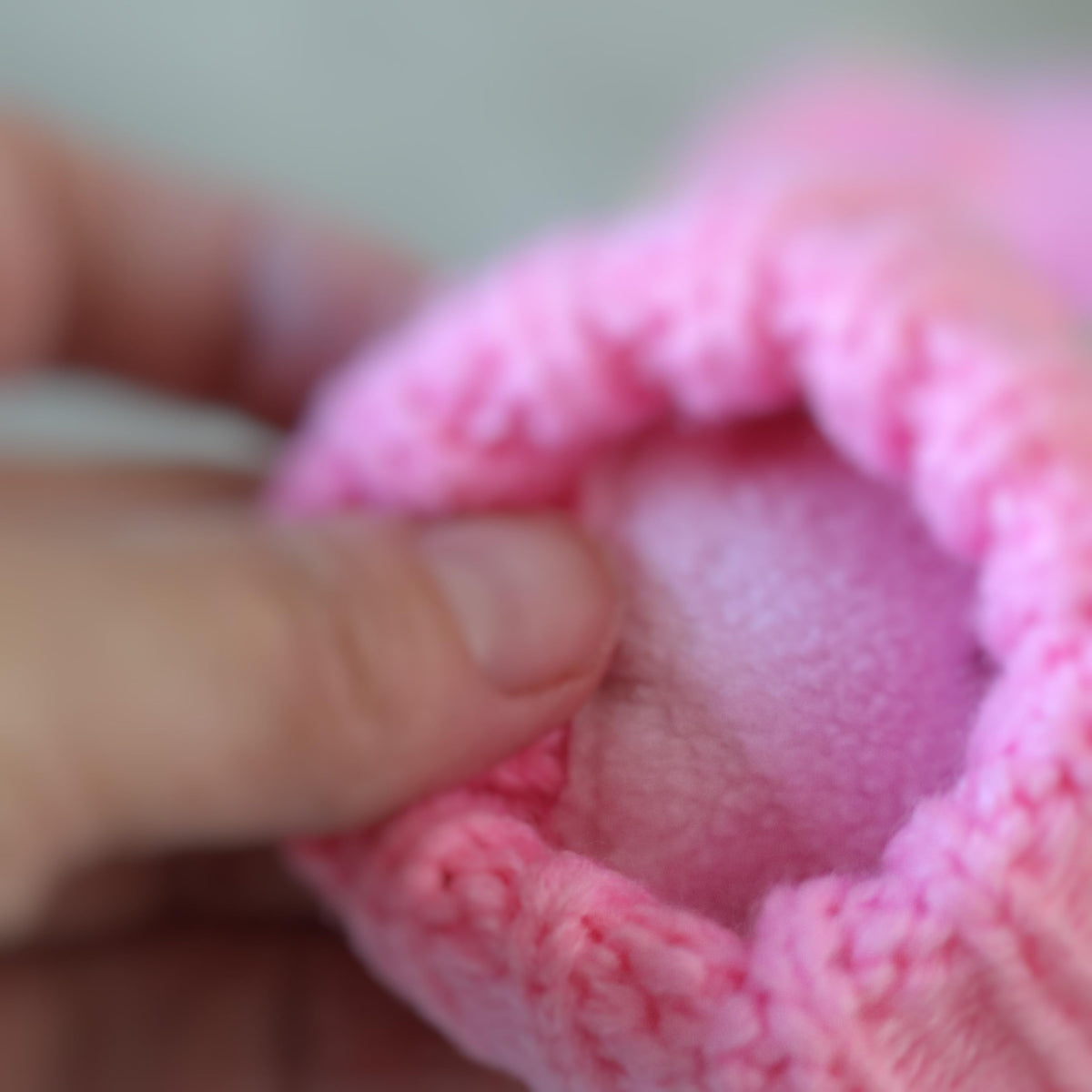 Pink fleece-lined knit mitten opening with soft inner lining, held in a hand (close-up).