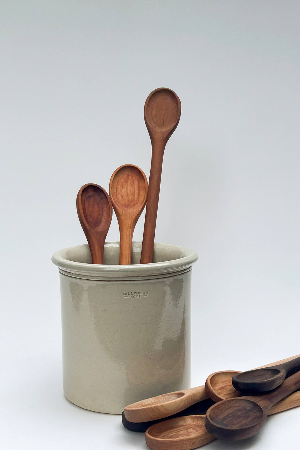 Assorted wooden spoons standing in a ceramic crock, oval bowls and long handles.