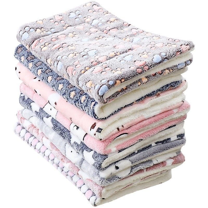 Folded pet mats stack in gray, pink, and cream with paw-print patterns