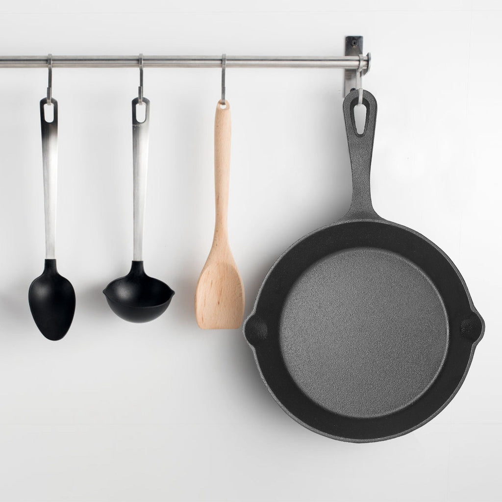Set of black cast iron skillets hanging on a rack with wooden and metal hooks