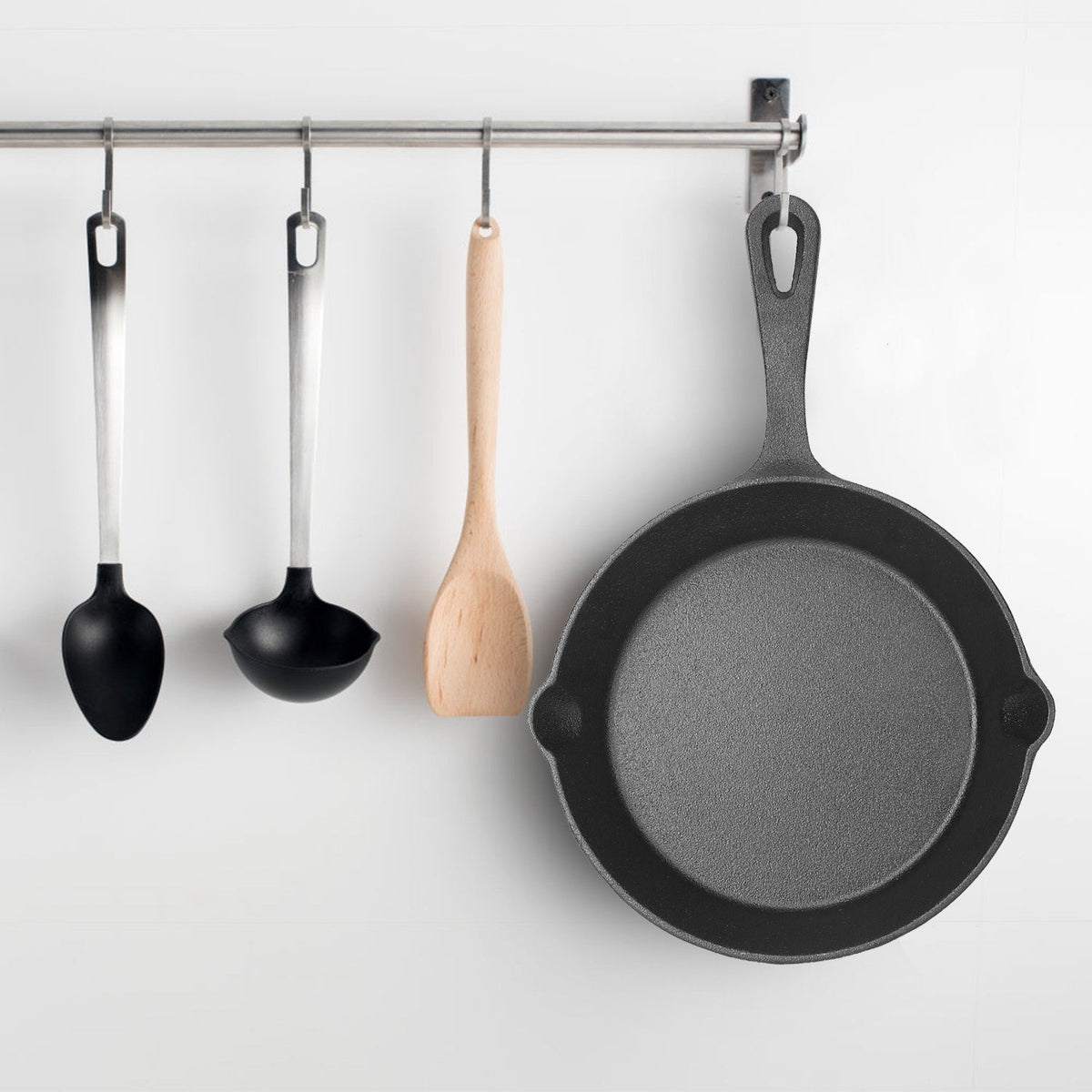 Set of black cast iron skillets hanging on a rack with wooden and metal hooks