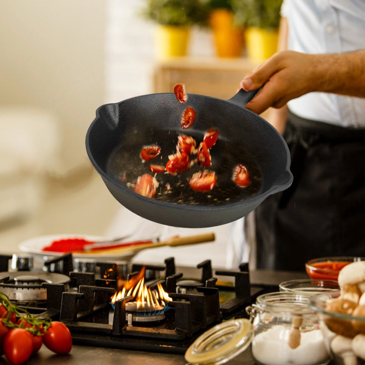 Hand holding a black cast iron skillet over a gas stove with shrimp and spices
