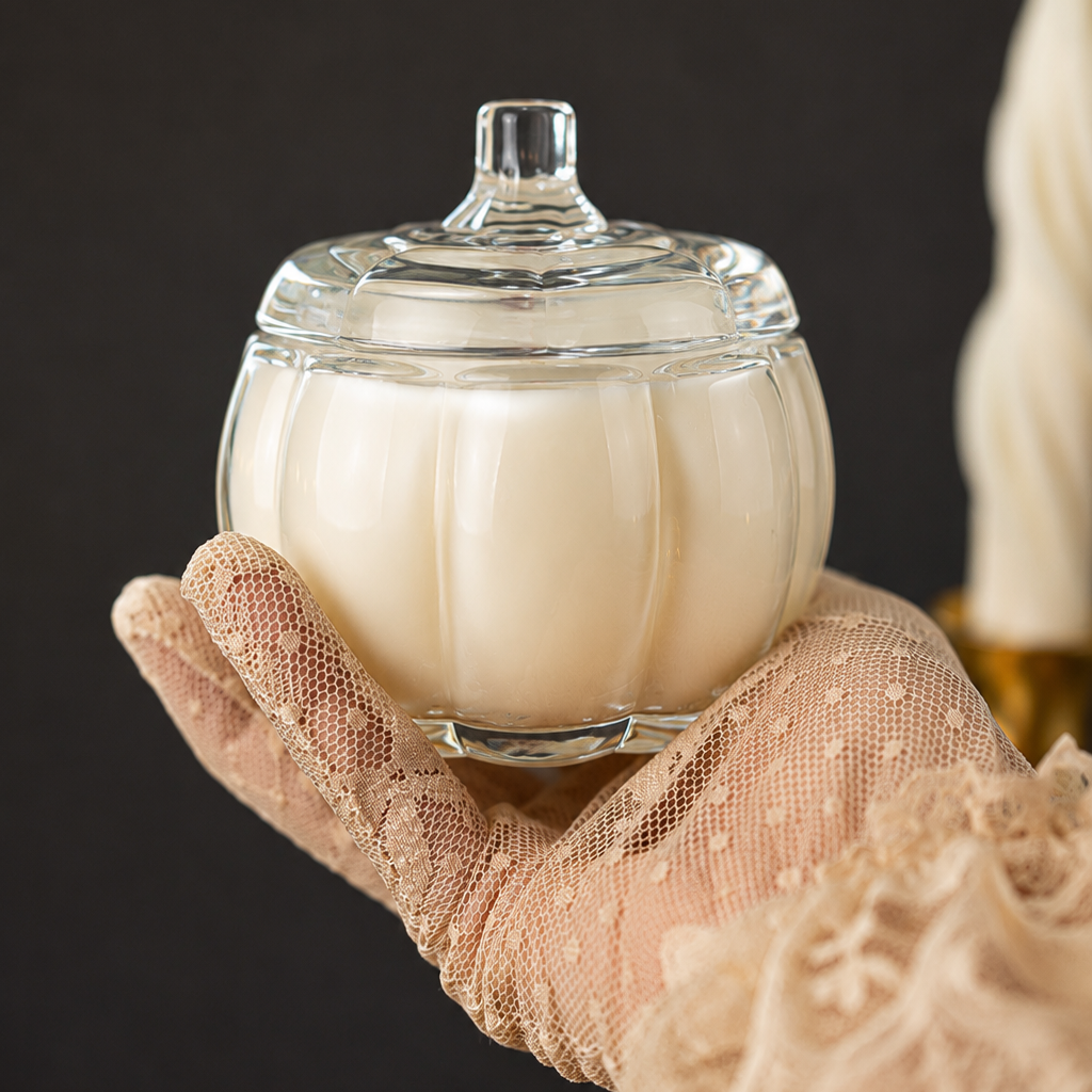Clear glass candle jar with cream wax, lid on top held by hands with net glove