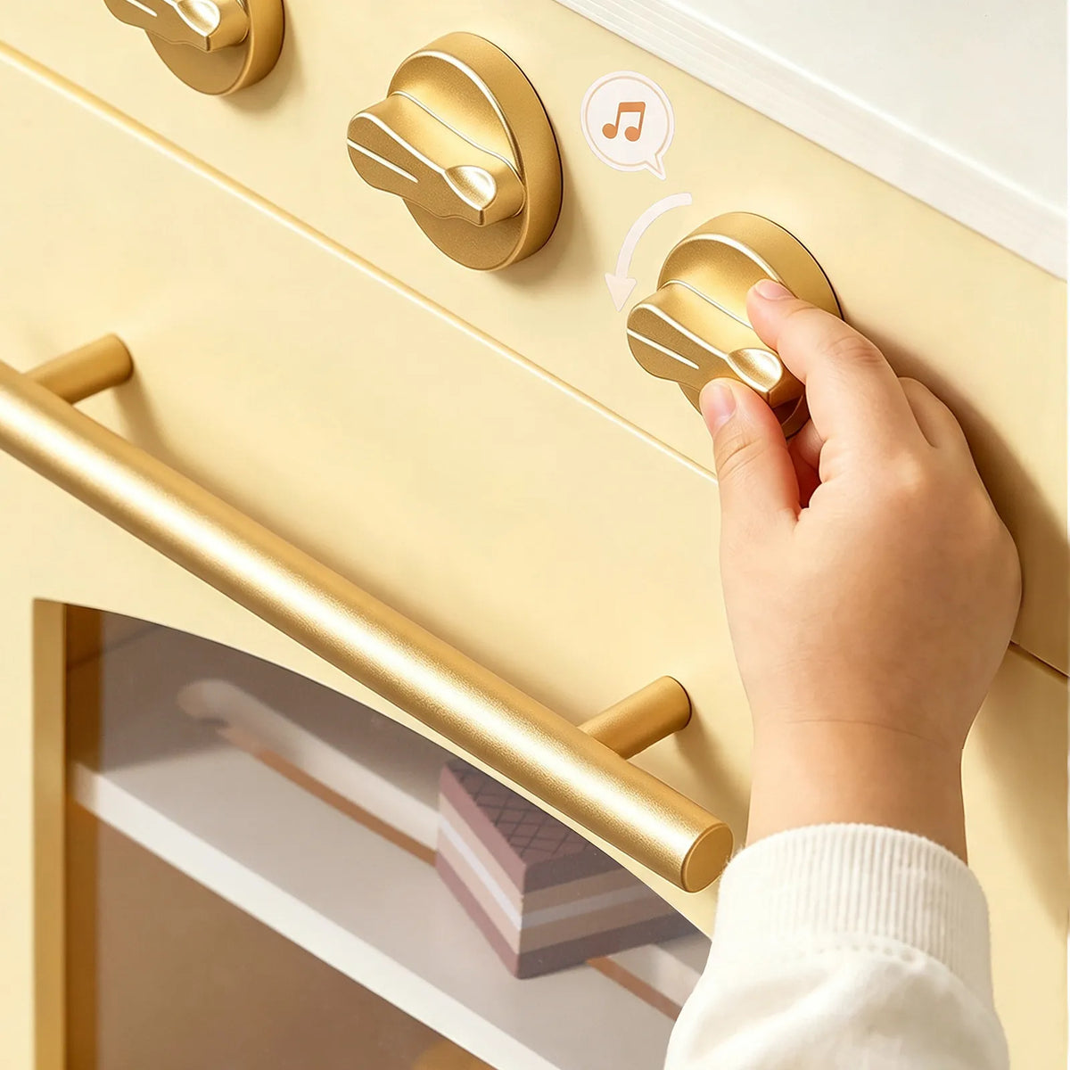 Child hand gripping gold cabinet knobs on a yellow wooden play kitchen