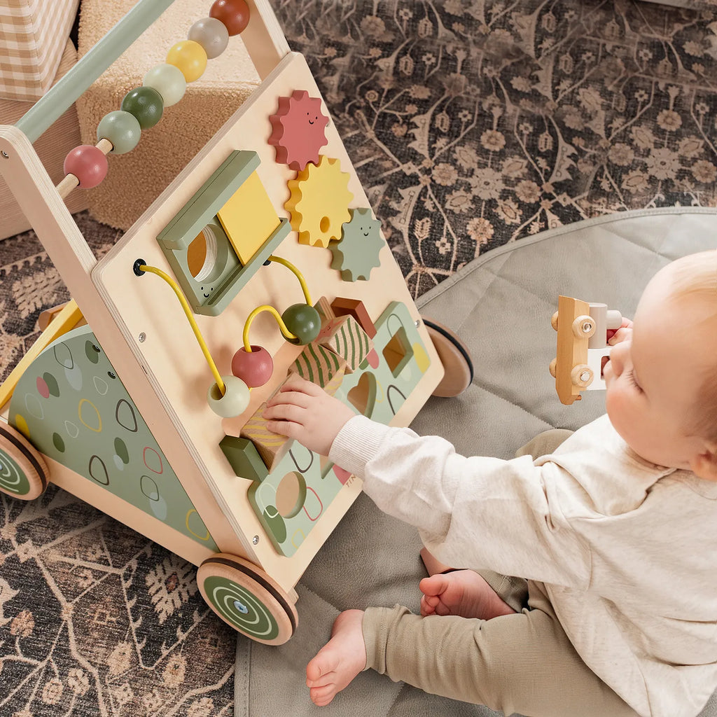 Baby playing with wooden activity walker featuring bead maze, mirror, and gear cutouts