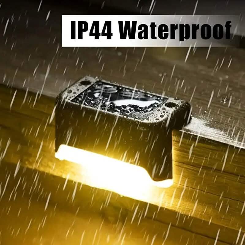 Waterproof solar deck light, black rectangular housing emitting warm glow in rain