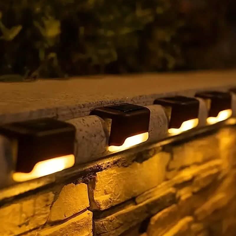 Solar deck lights set of four, black fixtures lining a stone walkway with warm light