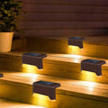 Four brown solar LED step lights with warm white glow on wooden steps