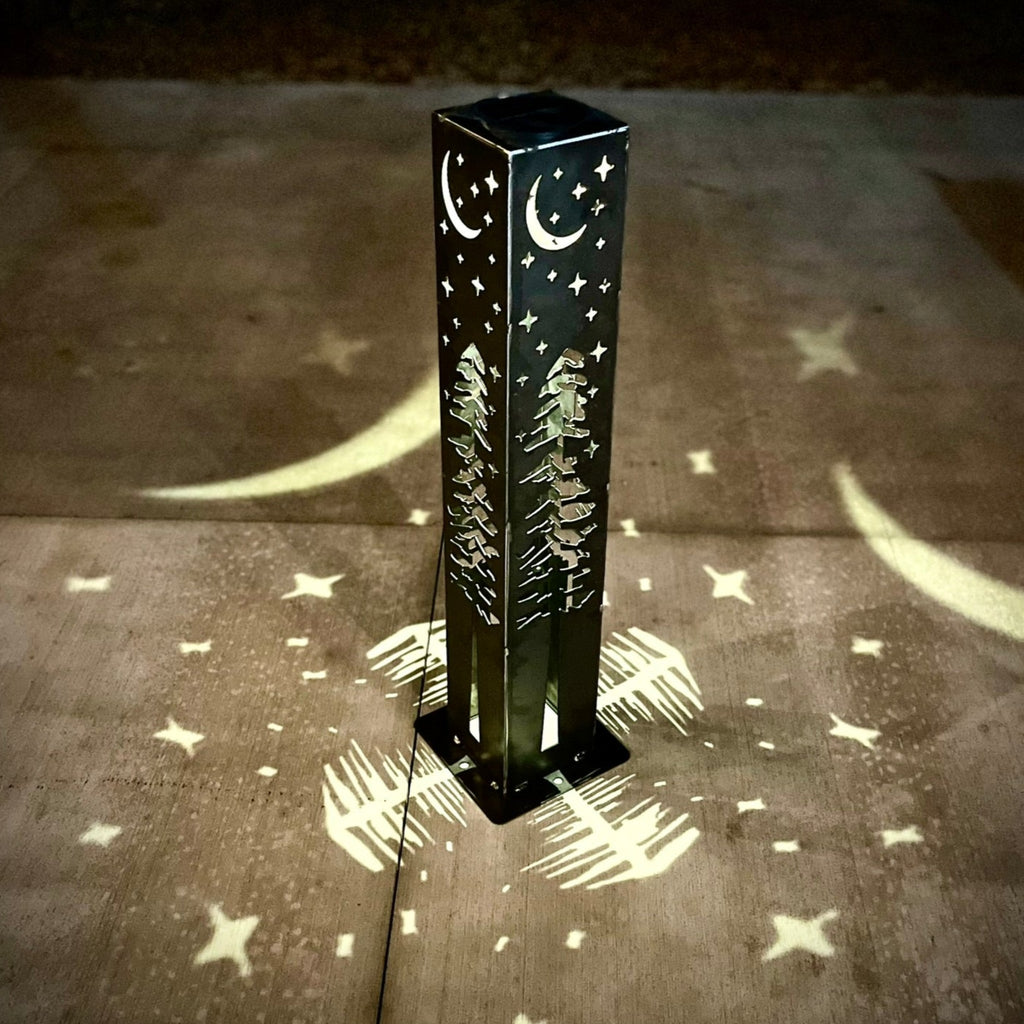 Solar light pillar on concrete with moon and star pattern cast in light at night.
