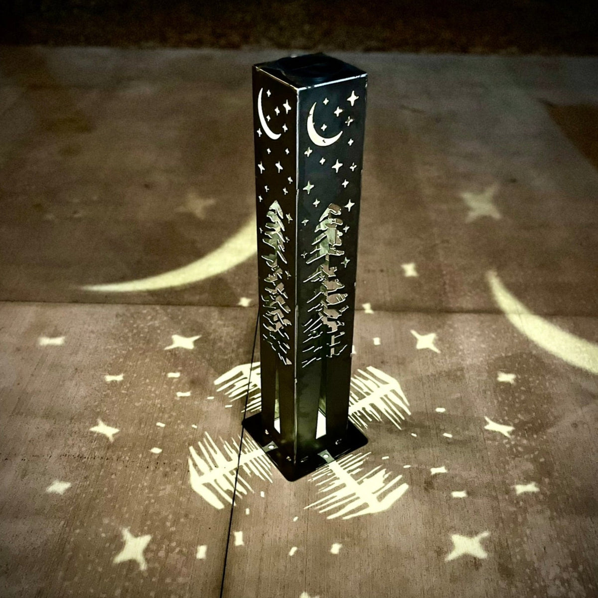 Solar light pillar on concrete with moon and star pattern cast in light at night.