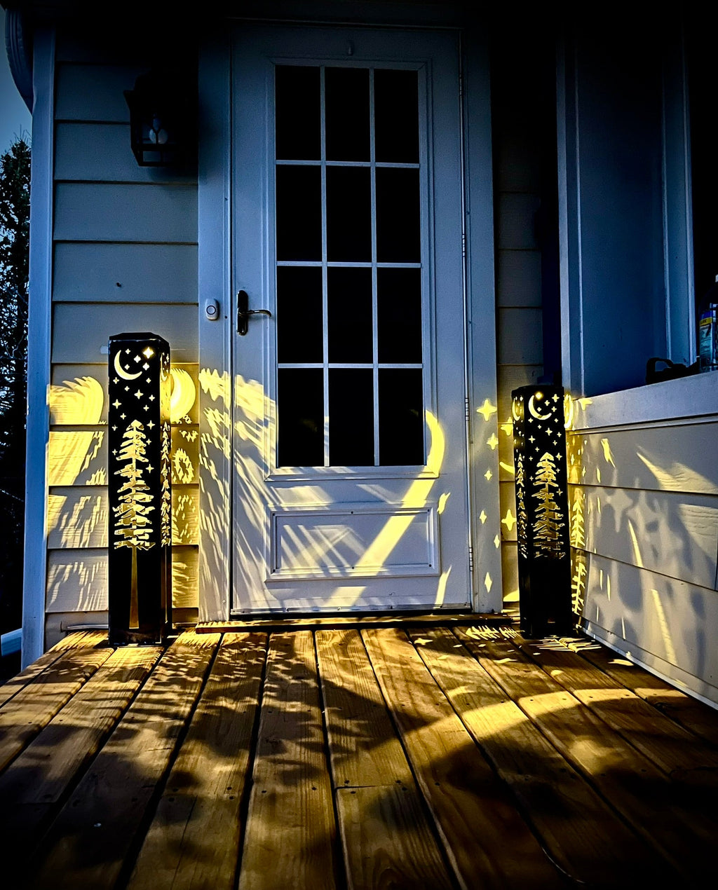 Silver solar light pillar lights up on a porch walkway with moon and star cutouts.