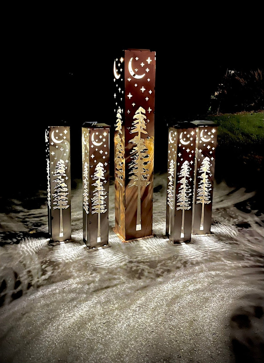 Group of solar light pillars with moon and stars cutouts, glowing over a driveway at night.