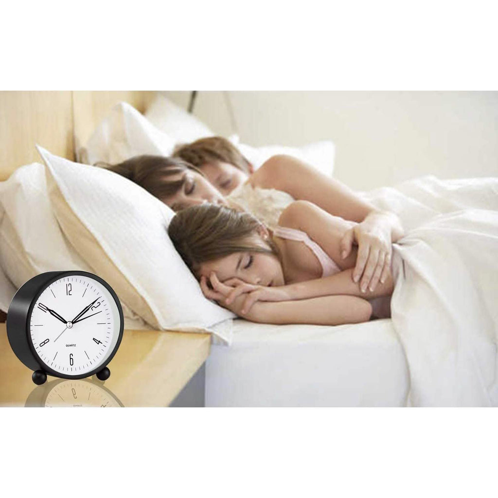 Black analog alarm clock on bedside setting with white face and twin bell feet