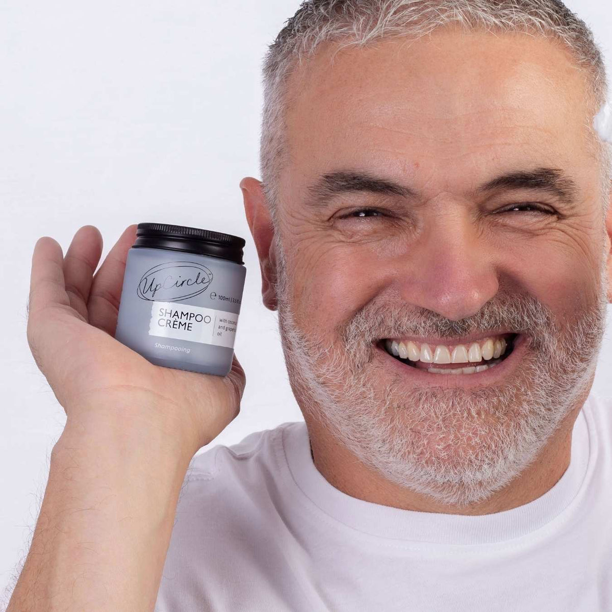 UpCircle shampoo creme jar held up by smiling man, light blue jar with black lid.