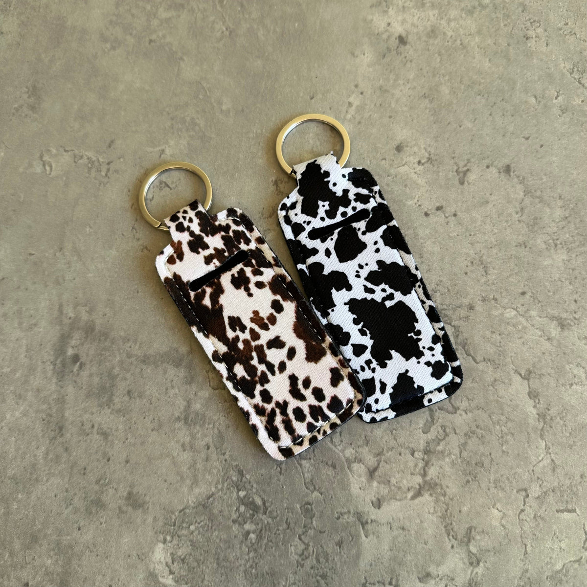 Cow print chapstick holder keychain pair with gold-tone key rings
