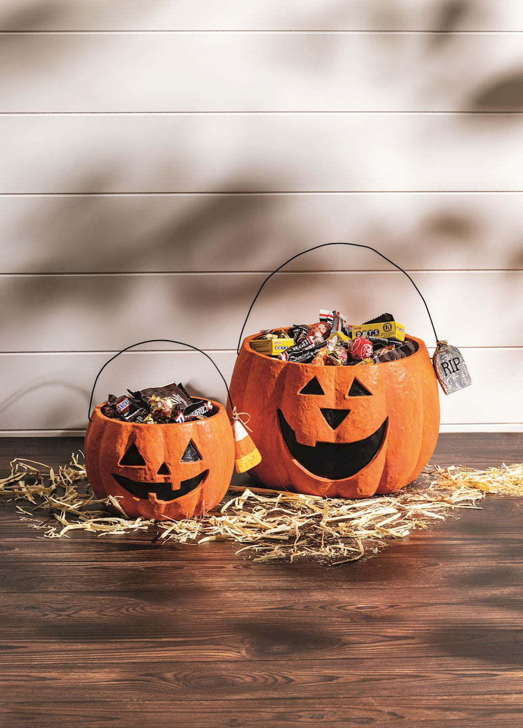 Pair of orange paper mache jack-o'-lantern treat buckets with handles, filled with candy