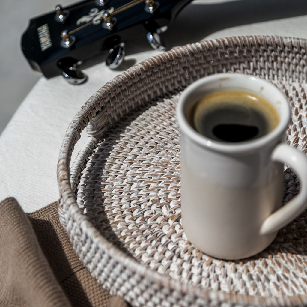 Round rattan tray holding a white mug of coffee, woven white finish