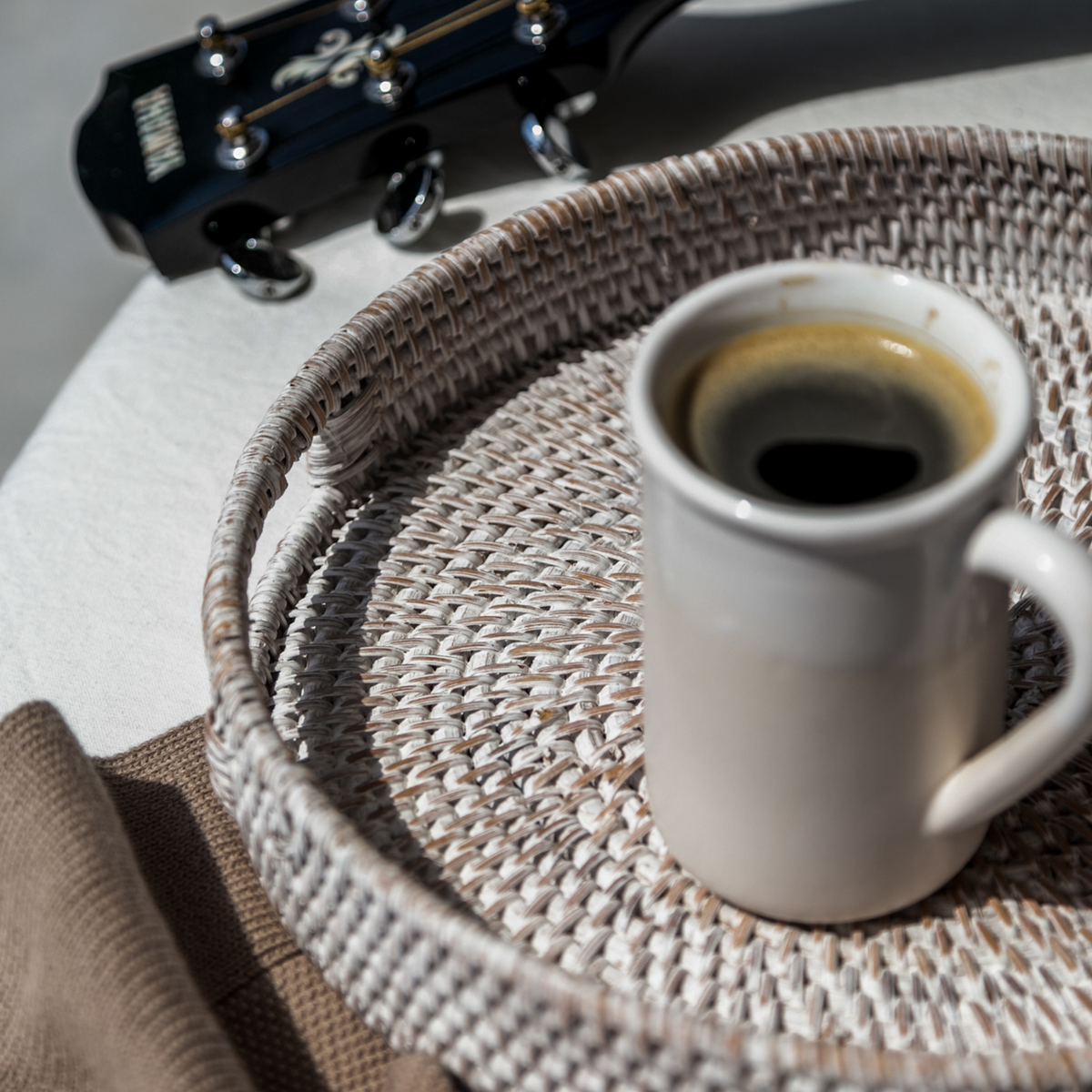 Round rattan tray holding a white mug of coffee, woven white finish