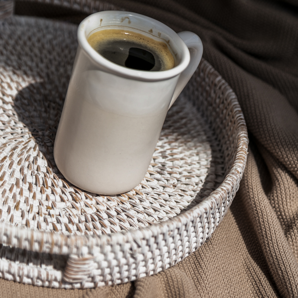 Round woven rattan tray with white mug and coffee, braided texture surface