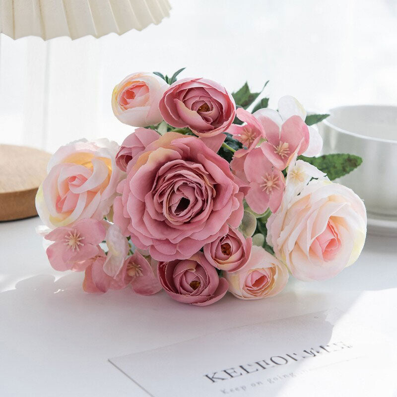 Pink and light pink silk rose bouquet with green leaves in a clear vase