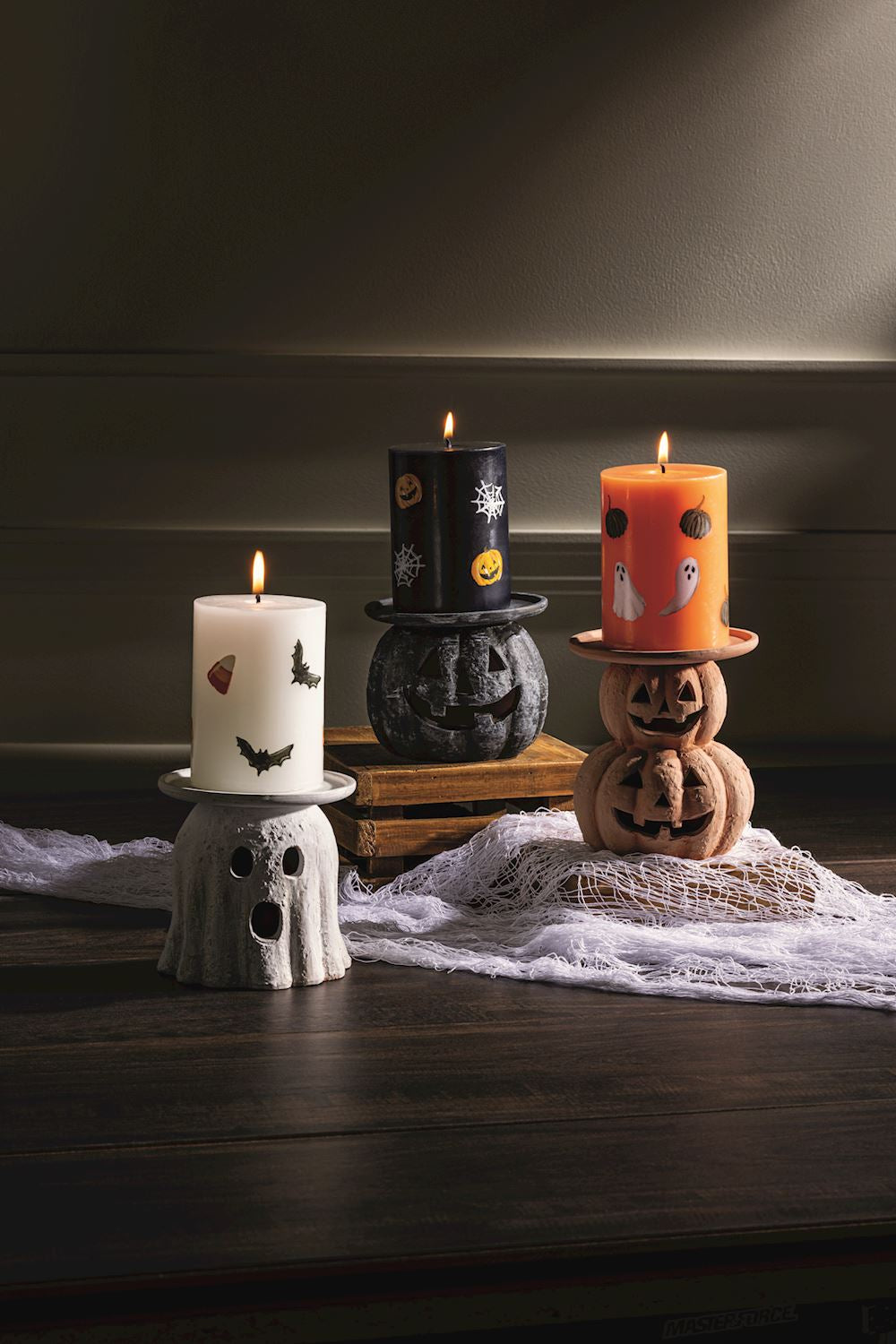Halloween pillar candle holders with lit candles: terracotta pumpkin, black, and white ghost designs