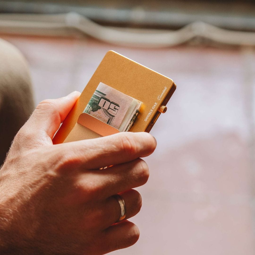 Tan pop-up cardholder held in hand with card and cash partially visible.