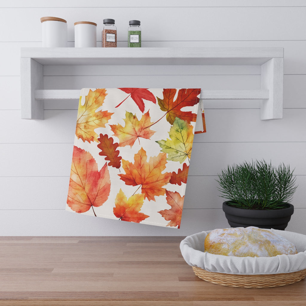 Autumn leaf print tea towel hanging on a kitchen shelf, rectangular white background