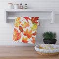 Autumn leaf print tea towel hanging on a kitchen shelf, rectangular white background
