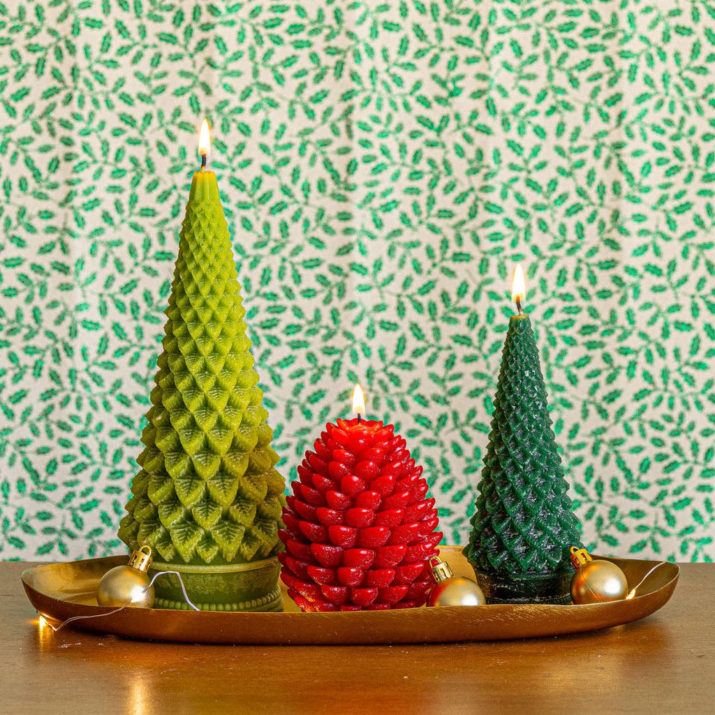 Tree-shaped candles on tray: red pinecone candle between two green candles, flames lit
