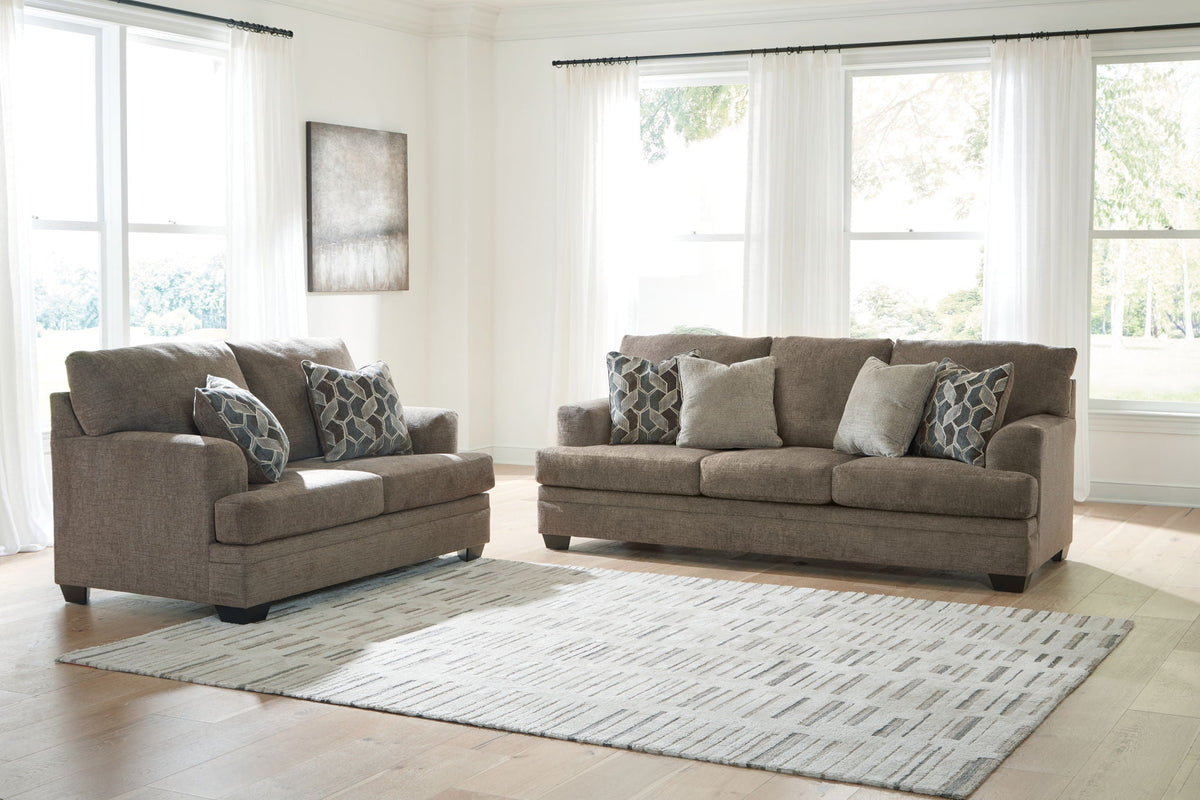 Tan fabric living room set with sofa, matching chair, and patterned accent pillows