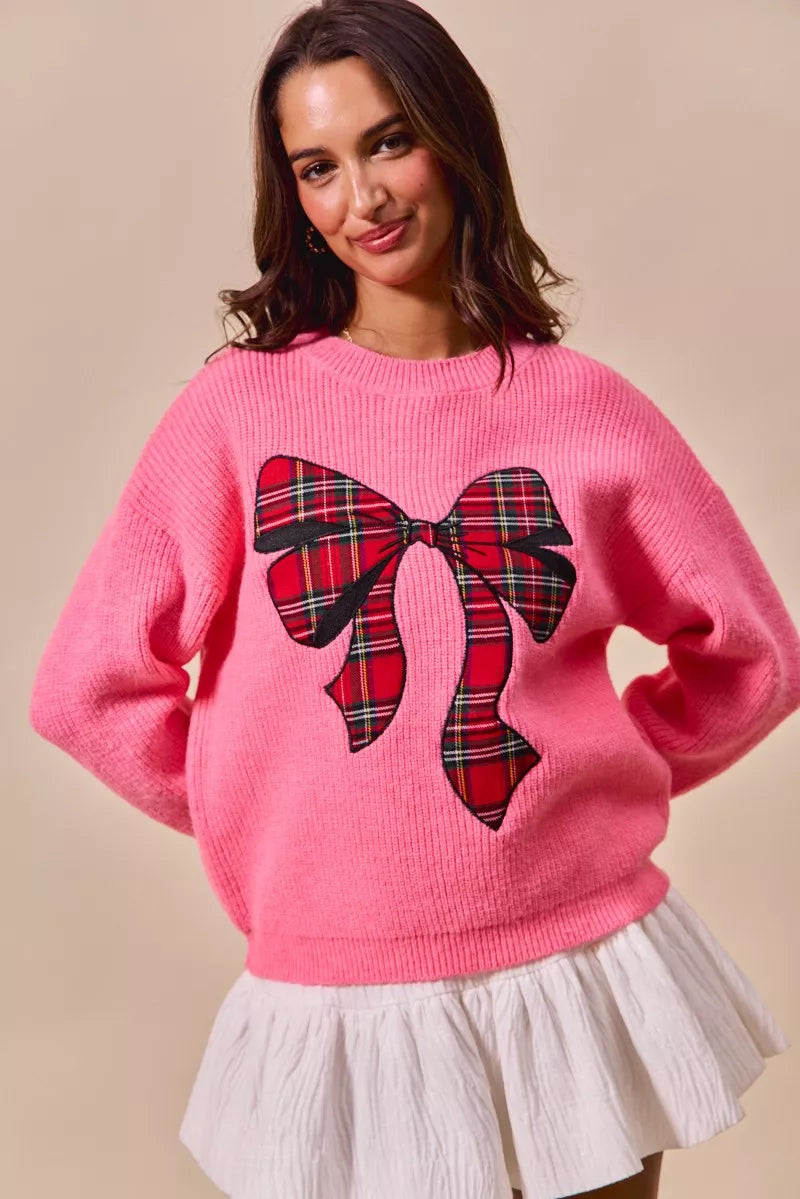 Pink holiday sweater with oversized plaid bow ribbon detail and crew neck