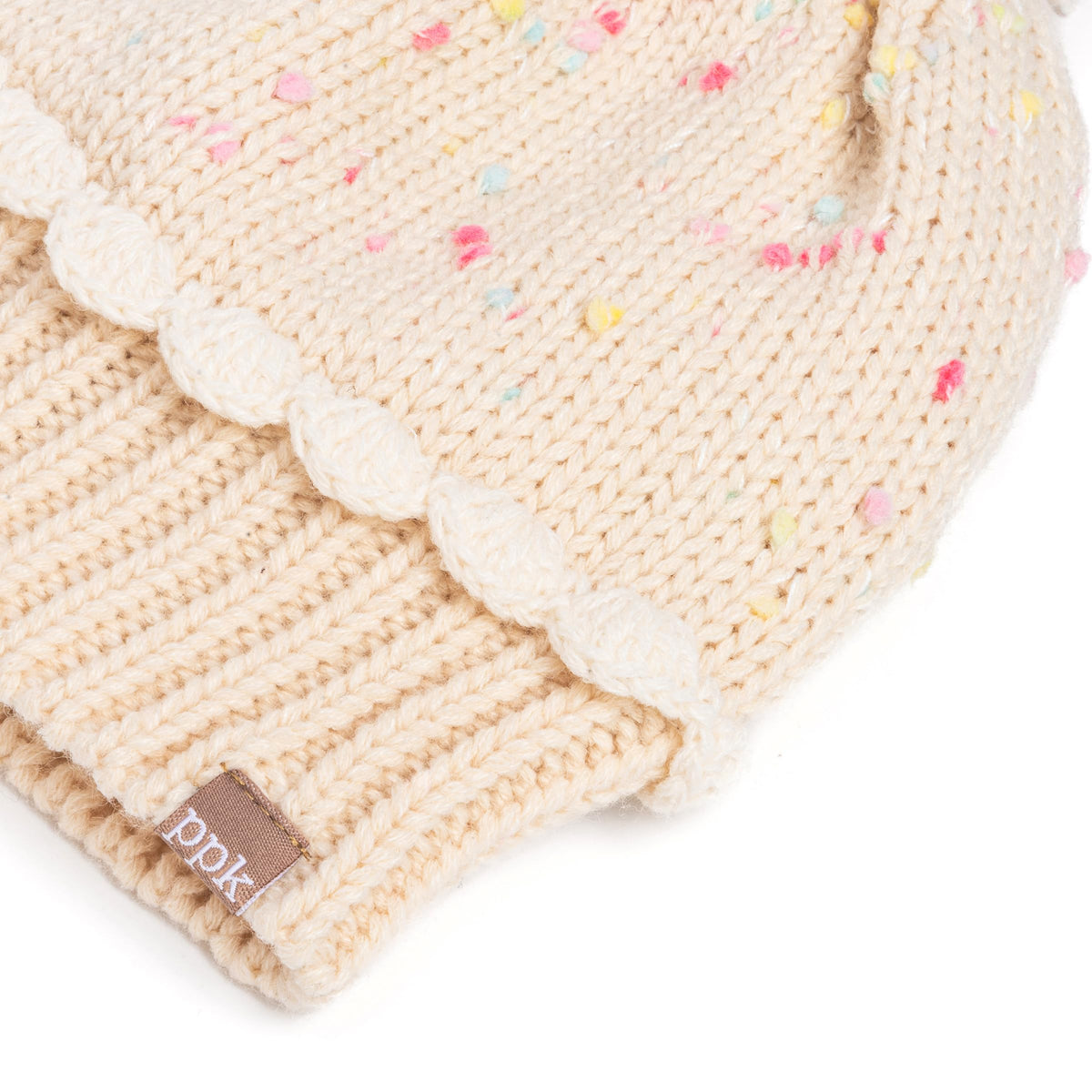 Cream knit beanie cuff detail with ribbed texture and brown leather brand patch.