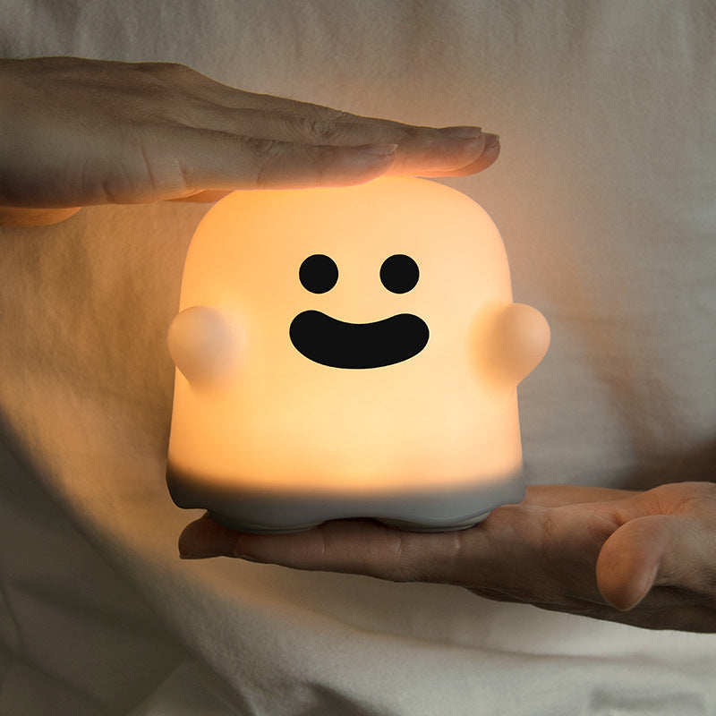 Hand-held silicone ghost night light lamp with smiling face, warm glowing LED light.
