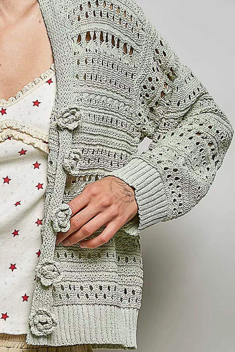 Close-up of light gray open-knit cardigan sleeve with crocheted floral textures