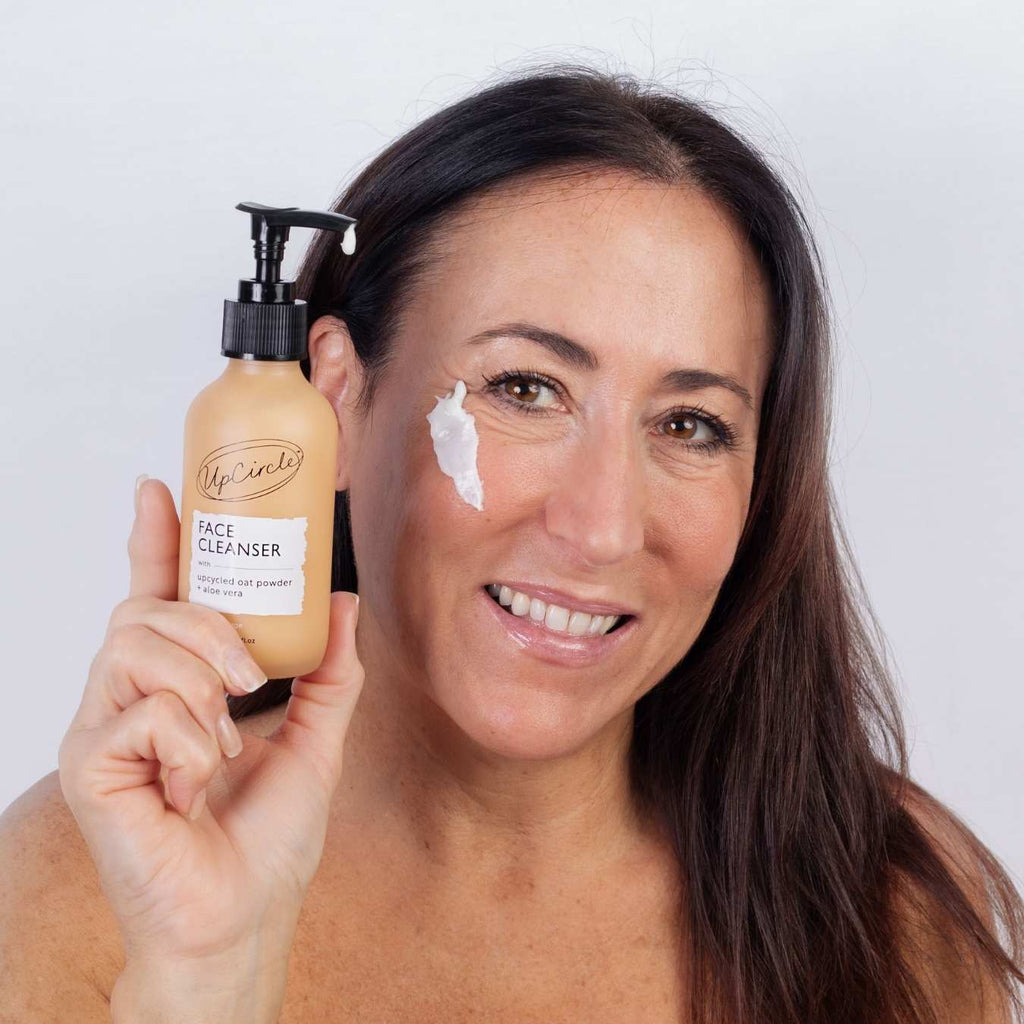 Woman holding cleansing face milk bottle with cream dab on cheek