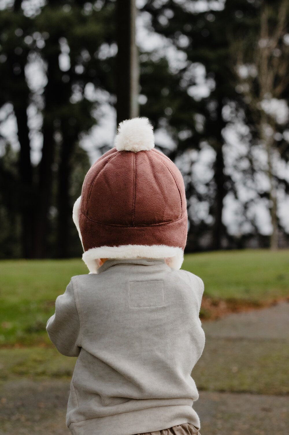 Kids trapper hat back view in brown with white faux fur ear flaps and pom-pom